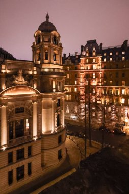 Klasik mimari ve kubbeli bir kuleye sahip Londra binası, bir sokak ve ağaçlarla aydınlık gökyüzüne karşı.