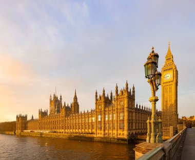 Westminster Sarayı ve Elizabeth Kulesi, İngiltere 'nin ikonik tarihi simgesi olan Thames Nehri üzerinde gün batımının sıcacık parıltısında parıldıyor.