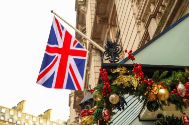 Geleneksel Noel çelenkleri, kırmızı böğürtlenler ve altın süslemelerle süslenmiş bir binanın girişinde dalgalanan Birleşik Krallık bayrağı, Londra 'da vatanseverlik ve tatil ruhunu ifade ediyor.