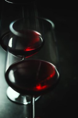 İki kadehte dönen kırmızı şarap koyu kırmızı renkleri ve kasvetli arka planda yansımaları vurguluyor.