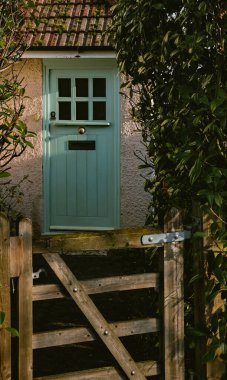 Kırsal ahşap bahçe kapısı ziyaretçileri hoş karşılıyor yemyeşil yeşilliklerin arasından yeşil kapılı ve desenli pencereli büyüleyici bir kulübeye.