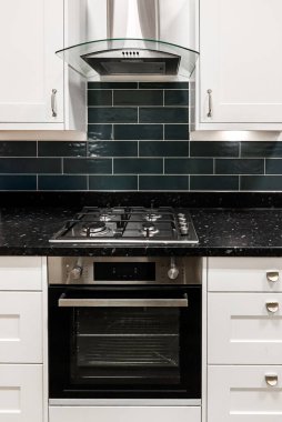 Modern mutfak iç mimarisi, beyaz dolap, paslanmaz çelik fırın, gaz hobisi, ve koyu fayanslı arka plan.
