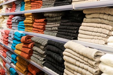 Raflara düzgünce dizilmiş yumuşak pamuk havlular, ev tekstil ve banyo ihtiyaçları için çeşitli renkler ve dokular sunuyor