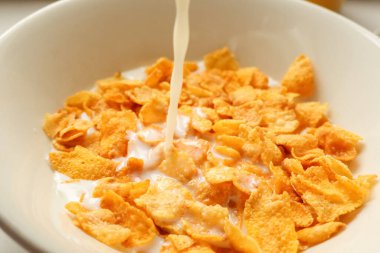 Beyaz bir kasede gevrek mısır gevreğinin üzerine süt dökülüyor. Hızlı, besleyici ve klasik bir sabah kahvaltısı hazırlıyorlar.