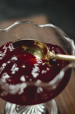 Kırmızı meyve reçeli cam bir tabağı dolduruyor, altın bir kaşık tatlı ve zengin meyve korumasına daldırıyor, yakın çekim