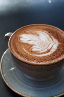 Süslü latte sanatıyla sıcak bir kahveyi kapatıyoruz, bir fincan tabağının üzerinde oturuyoruz, sıcak bir mola ya da sabah ritüeli için mükemmel.