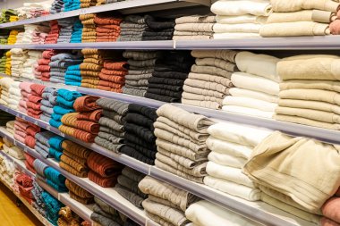 Katlanmış tekstil havlularının bir mağaza ortamında raflarda düzenlenmiş çeşitli renk ve malzemelerle perakende seçimi gösteriliyor
