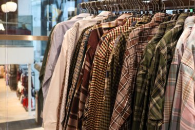 Damgalı gömlekler askılara güzelce asıldı, şık giyim seçenekleri sergilendi ve şık bir butik ortamında perakende fırsatları sunuldu.