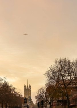 Londra 'daki Westminster Sarayı ve At Muhafızları Geçidi' nin Elizabeth Kulesi 'nin üzerinde turuncu bir gökyüzünde uçan uçak.