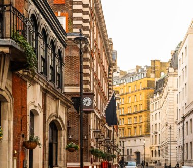 Londra caddesinde tuğla cepheli klasik İngiliz mimarisi, süslü detaylar, geleneksel saat ve şehir hayatı sergileniyor.