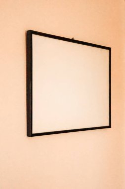 Açık şeftali rengi bir duvarda asılı siyah kenarı olan boş bir çerçeve tasarım modelleri için boş kopya alanı sağlıyor