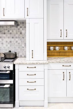 Beyaz sallanan dolaplar, kahverengi kulplar, mozaik döşemeler ve açık granit tezgahlı temiz modern mutfak.