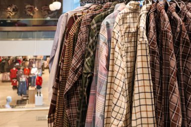 Parlak bir giyim mağazasının rafında asılı duran ekose gömlekler, modern moda perakendecisi için çeşitli desenler ve renkler sergiliyor.