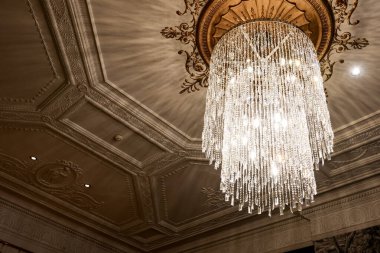 Karmaşık alçı detaylarıyla süslü bir tavandan sarkan kristal avize, ışığı yansıtıyor ve sofistike, varlıklı bir atmosfer yaratıyor.
