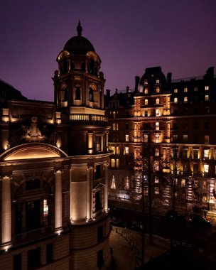 Alacakaranlıkta Londra şehir manzarası, mor gökyüzüne karşı aydınlatılmış, kubbeli klasik bir bina. Şehir gece mimarisi