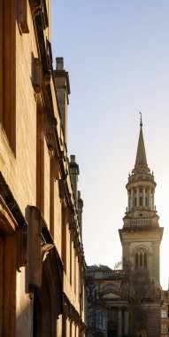 Açık gökyüzünün altındaki All Saints Kilisesi 'nin belirgin kulesiyle çelişen bir üniversite binasının tarihi taş cephesi.