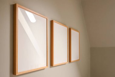 Wooden frames with blank white canvases hanging on a light wall, providing a modern empty exhibition space mock up