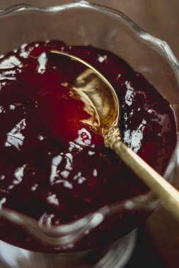 Cam bir tabakta kırmızı böğürtlen reçeli, tatlı meyvelerin arasında duran zarif bir altın kaşık. Ev yapımı tatlıyı hazırlıyorum.