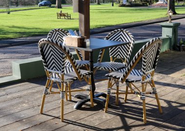 Ahşap bir verandada dört siyah-beyaz sandalyeli Bistro masası, park tarafındaki içeceklerin tadını çıkaran müşteriler için hazır.