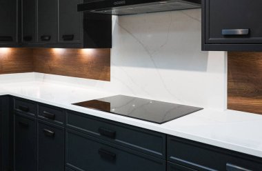 Karanlık dolaplar, beyaz kuvars yüzeyi ve sofistike ev tasarımı sağlayan sıcak ahşap aksanlı modern mutfak tasarımı.