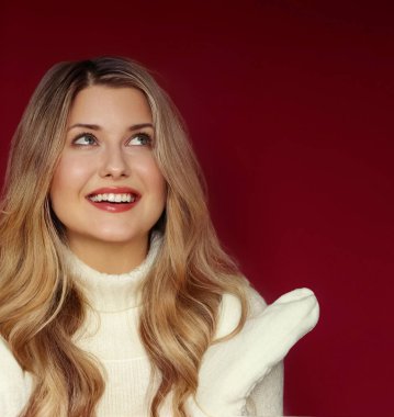 Kocaman gülüşü olan mutlu sarışın kadın yukarı bakıyor, sıcak beyaz bir kazak ve eldiven giyiyor, kış neşesini sergiliyor.