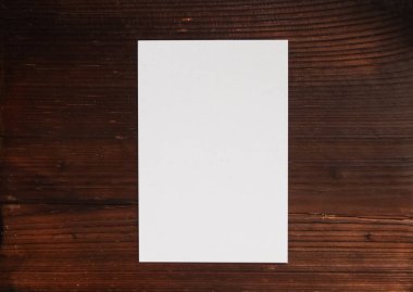 Boş beyaz kağıt ve koyu kahverengi ahşap bir masaüstüne boş kırtasiye malzemesi, maketler için ideal bir arkaplan oluşturur