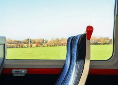 Tren yolcusu, İngiltere 'nin Hertfordshire kentindeki konforlu pencere kenarından yeşil tarlaların, ağaçların ve uzak evlerin manzarasının keyfini çıkarıyor.