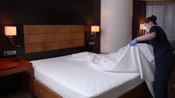 Pokojówka w masce i rękawiczkach ścieli łóżko w sypialni — Wideo stockowe