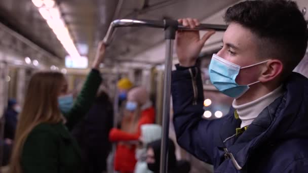 Wysoki młody człowiek w masce twarzy jadący pociągiem metra — Wideo stockowe