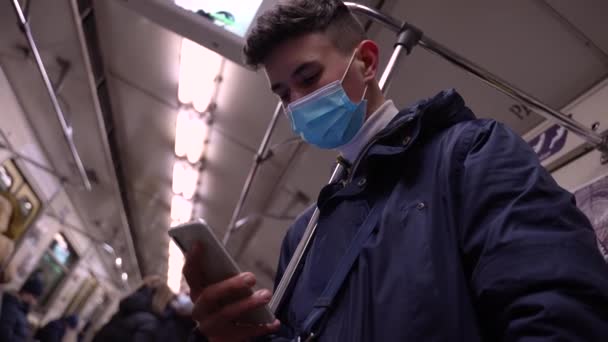 Tiener jongen in het gezicht masker met behulp van telefoon rijden in de metro — Stockvideo