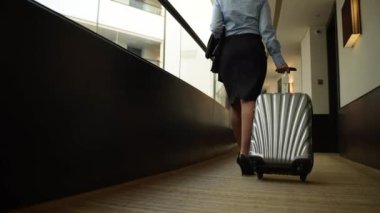Bavullu bir kadın otel koridorunda yürüyor.