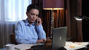 Telefonla ve dizüstü bilgisayarla meşgul bir kadın evde çalışıyor.