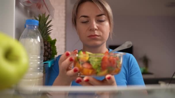 Slimme vrouw eet smakeloze salade aan de koelkast — Stockvideo