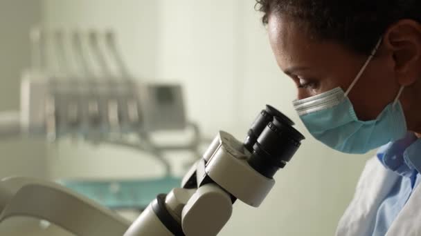 Dentista enmascarada usando microscopio durante el trabajo — Vídeos de Stock