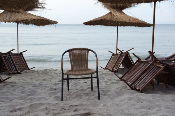 Az esti beach, nádfedeles napernyők és magányos szék — Stock Fotó