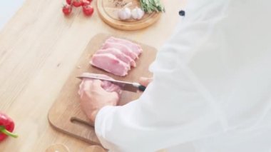 Sebzelerin yanında domuz filetosu doğrayan şefin kırpılmış görüntüsü.