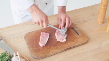 Beyaz masada domuz eti doğrayan şefin kırpılmış görüntüsü.