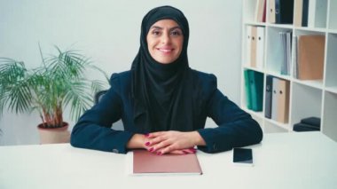 Ofiste kağıt klasörü ve akıllı telefonun yanında gülümseyen Müslüman iş kadını 