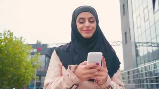 Mujer Musulmana Sonriente Usando Teléfono Inteligente Mientras Camina Aire Libre — Vídeos de Stock
