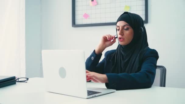 在办公室使用笔记本电脑的戴耳机的穆斯林女商人 — 图库视频影像
