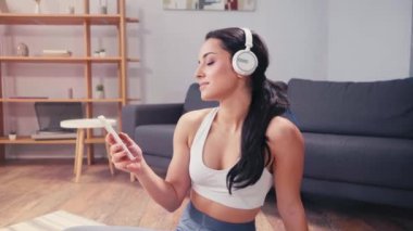 Gülümseyen sporcu kadın akıllı telefon ve kulaklık kullanıyor. 