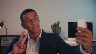 Duygusal Afrikalı Amerikalı iş adamı selfie çekiyor ve zafer işareti gösteriyor. 
