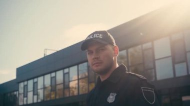 Şapkalı ve üniformalı bir polis memuru dışarıdaki kameraya bakıyor. 