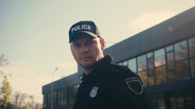Üniformalı, kendinden emin bir polis dışarıdaki kameraya bakıyor. 