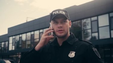 Üniformalı ve şapkalı bir polis şehir caddesinde akıllı telefondan konuşuyor. 