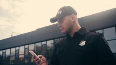 Şehir caddesinde akıllı telefon kullanan genç bir polis. 