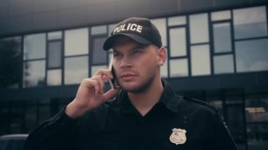 Üniformalı ve rozetli bir polis şehir caddesinde akıllı telefondan konuşuyor. 
