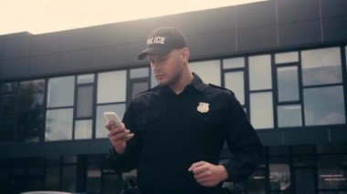Polis memuru binanın yakınında akıllı telefon kullanıyor. 