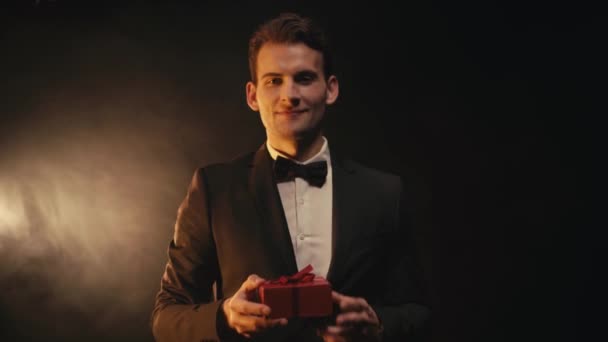 Εστίαση Έλξης Χαμογελαστός Νεαρός Άνδρας Κοστούμι Δείχνει Κόκκινο Κουτί Δώρου — Αρχείο Βίντεο