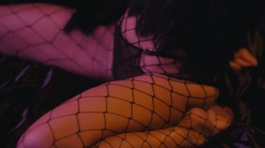 Fishnet taytlı seksi kadın siyah arka planda vücuda dokunuyor.